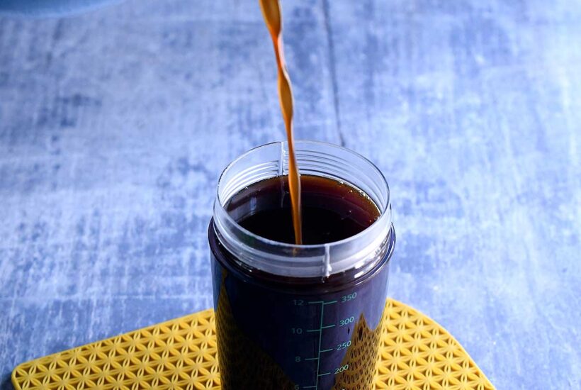 Strained vegan pumpkin spice syrup pouring into an OXO salad dressing container
