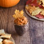 Ancho chile pumpkin hummus in a brown handforn potter bowl with a maple leaf shaped yellow tortilla chip