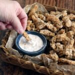 Air fryer soy curls made into clam strips being dipped into vegan tartar sauce.